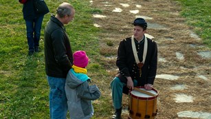 A man in blue Union uniform and drum speaking with three children.