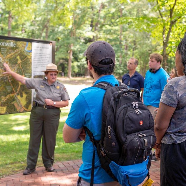 A park ranger speaking at a battle map to a group of older teenagers.