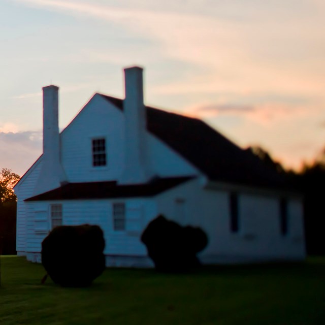 A small, white house with a-frame roof at sunset.