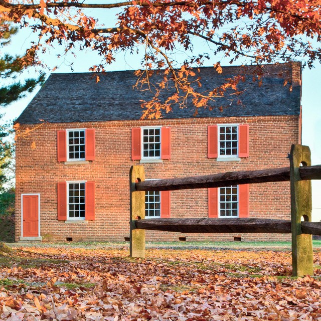 A two-story brick church with red shutters and a-frame roof in the fall.