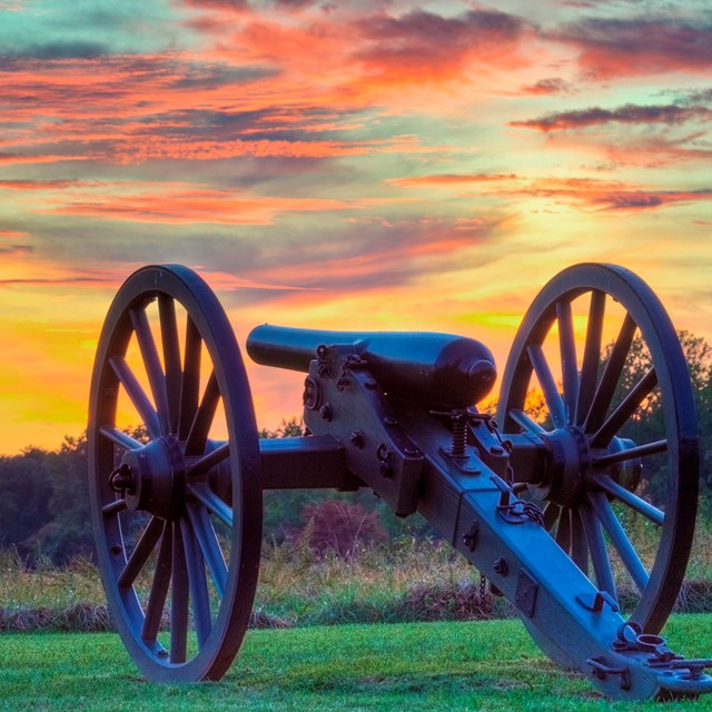 Cannon sits on field below a sunset.