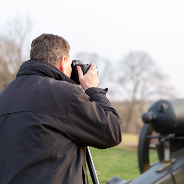 A man taking a picture near a cannon.