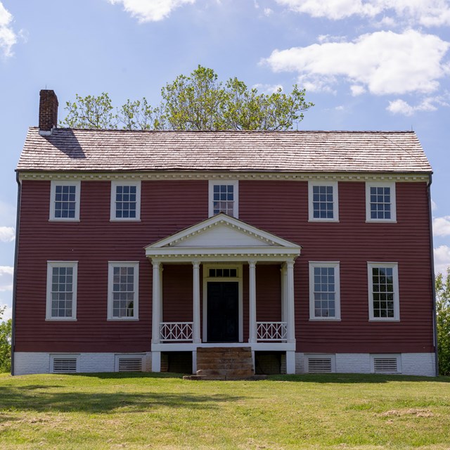 A two story red manor house with entrance columns.