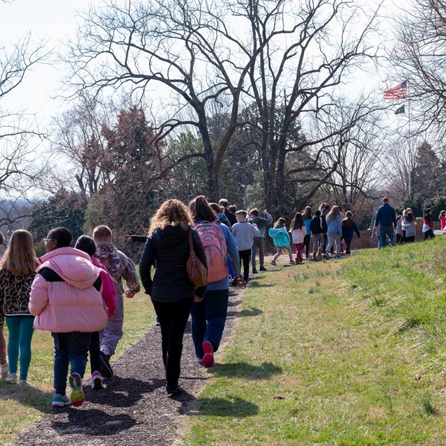 A large group of children and adults walk on a trail 