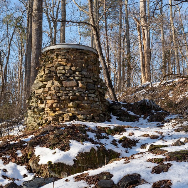 Remnants of a stone furnace, cylindrical and slightly narrower at the top, with light snow.