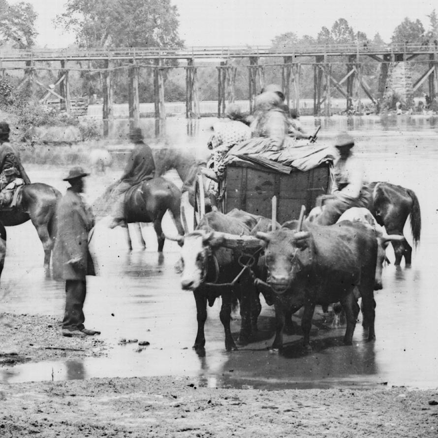 Historical photo of a group of enslaved people crossing a river.