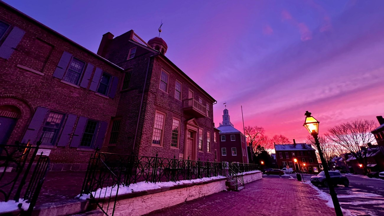 An old brick courthouse with a purple sunset sky some snow is on the ground