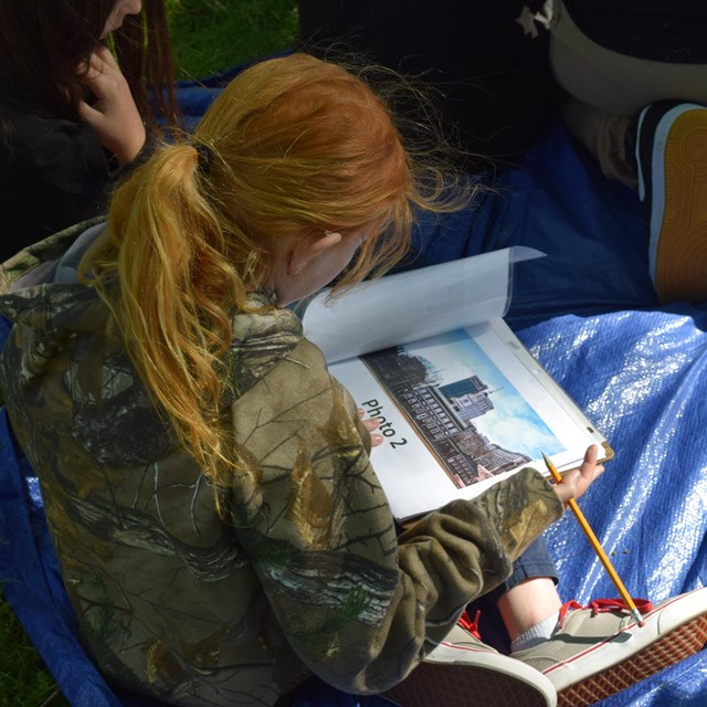 A student is sitting on the ground reading the instructions on her worksheet.