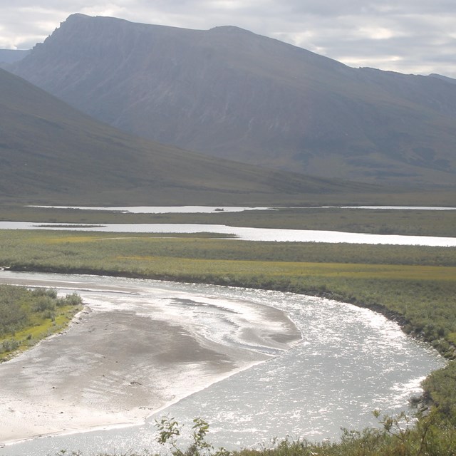 River winds through a broad green valley, mountains rise in the distance