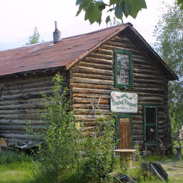 Two story log cabin with a sign on its front: Wiseman Trading Company