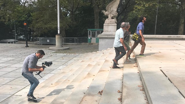 A videographer films a three people walking up the stairs of the Mausoleum