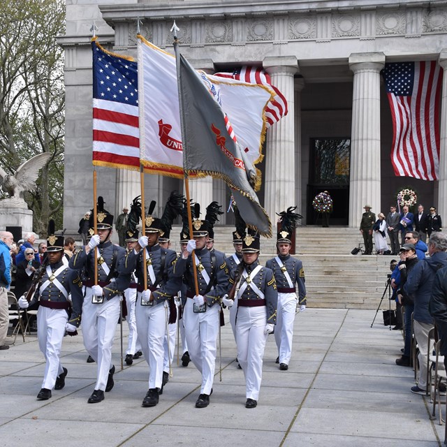 West Point cadets marching with flags in uniform in front of tomb