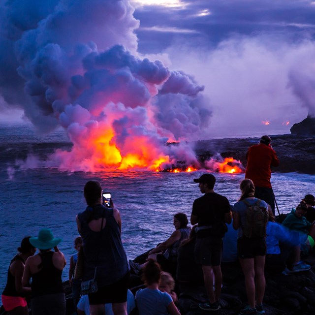 evening scene of molten lava entering the ocean, steam rising, people watching