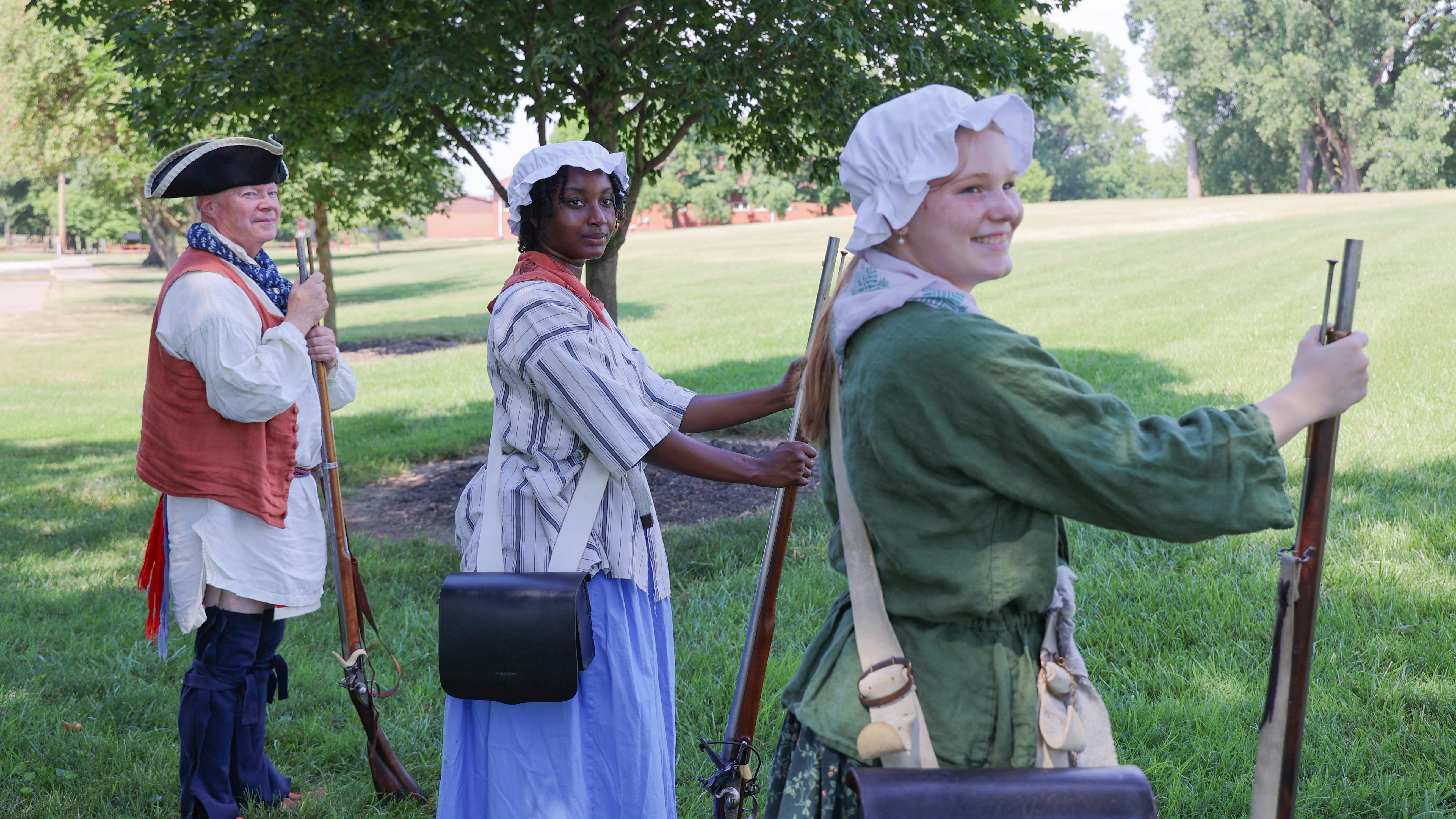 Three people in historic dress holding muskets waiting to start a historic weapons demonstration.