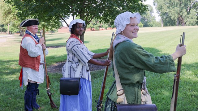 Three people in historic dress holding muskets waiting to start a historic weapons demonstration.