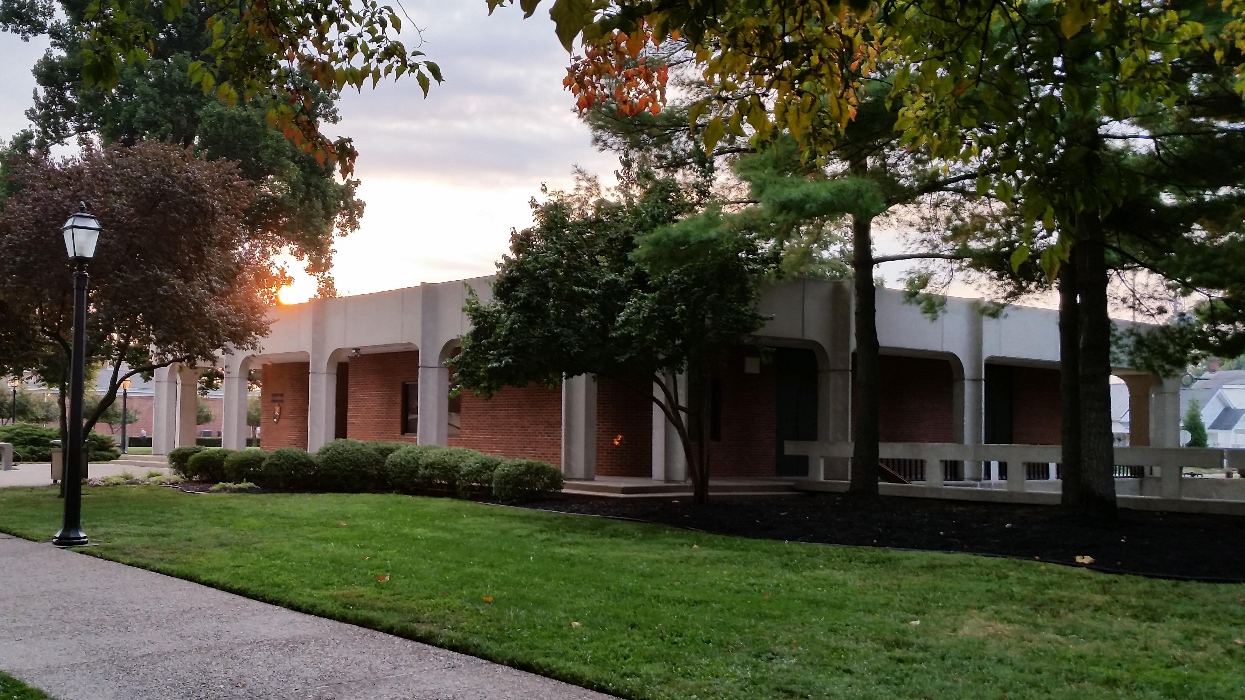 a small, square, brick and concrete, brutalist style building surrounded by trees and grass.  