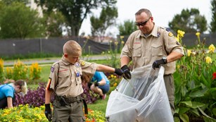 Boy scout and leader filling a garbage bag