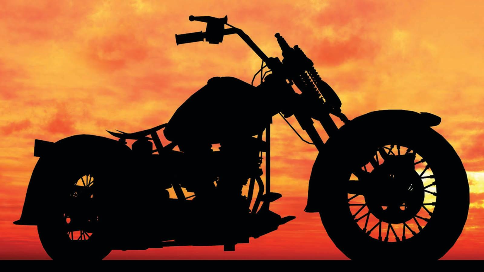 A black silhouette of a motorcycle stands in contrast to a bright orange and red sunset.