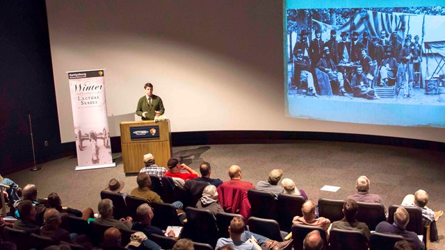 A park ranger, standing behind a podium, delivers a presentation in a theater.
