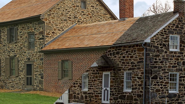 Historic brick and stone home surrounded by green grass and trees in the distance.
