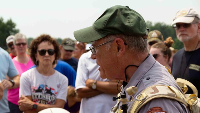 A park ranger speaks to a large group of visitors outside in a field.