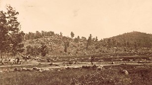 A black and white photo of a rocky hill in the distance and a rock strewn field in front.