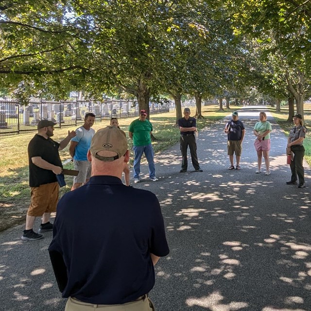 Eighteen adults gathered in a circle share stories in the National Cemetery.