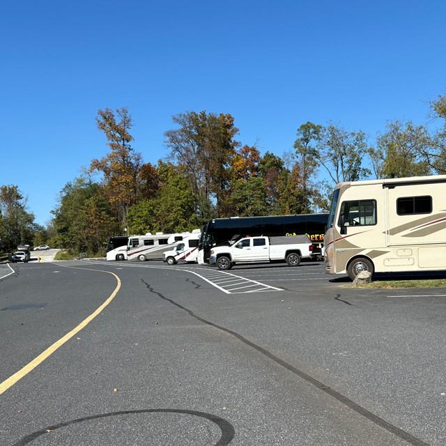 A parking lot showing a row of buses and RVs parked along the right of the picture..