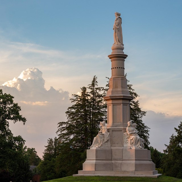 A large stone monument with trees and clouds on a blue sky in the background.