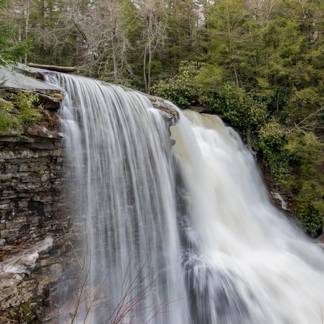 Waterfall with flowing river spilling over large body of rocks. 