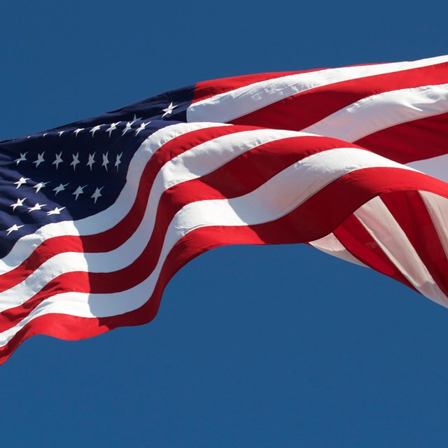 Red, white and blue flag blowing in the wind on a flag pole. Blue sky in background. 