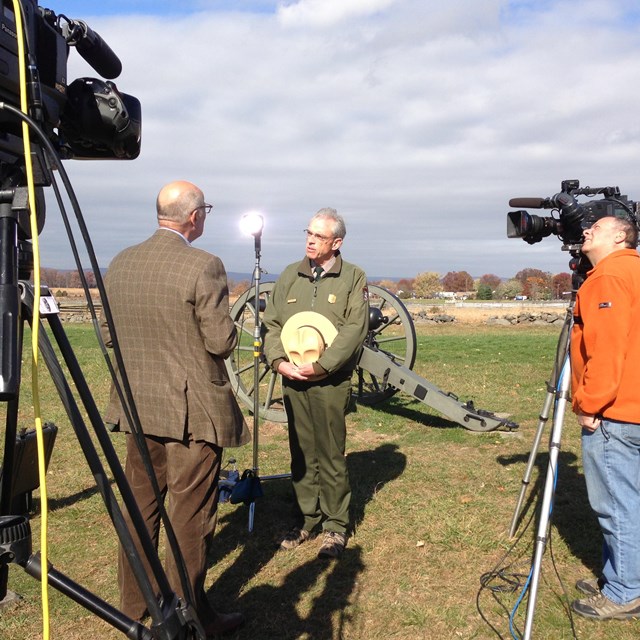 A park ranger stands on the battlefield conducting an interview with the media.