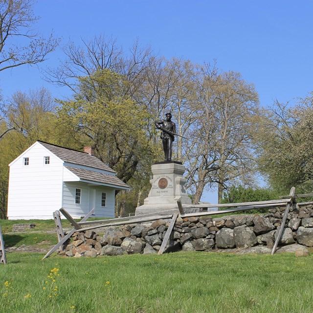 A battlefield scene with two monuments, a stone wall, and the small white Abraham Bryan house.