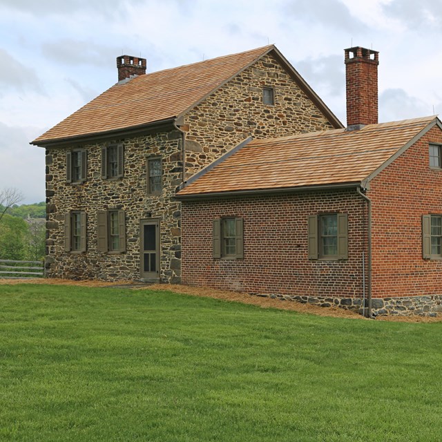 Historic brick and stone home surrounded by green grass and trees in the distance.