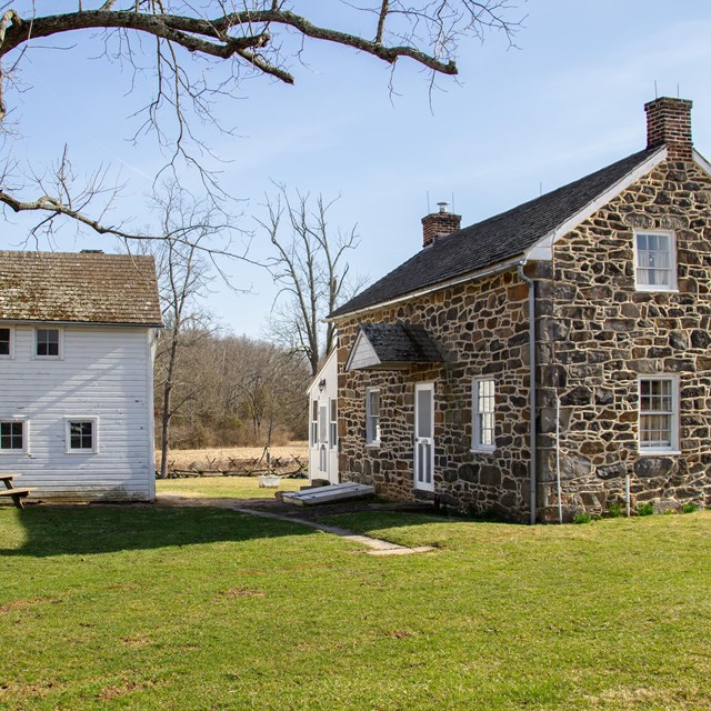 A stone building sits near a white wooden barn. 