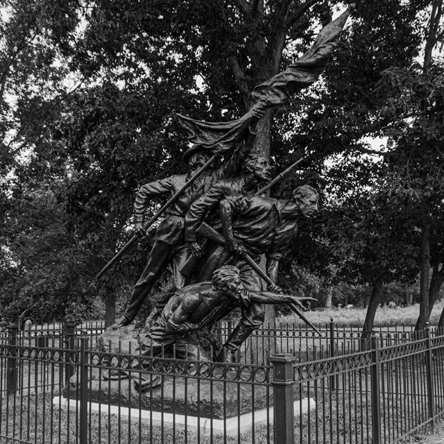 A black and white photo of a monument of four men charging forward holding weapons and a flag.