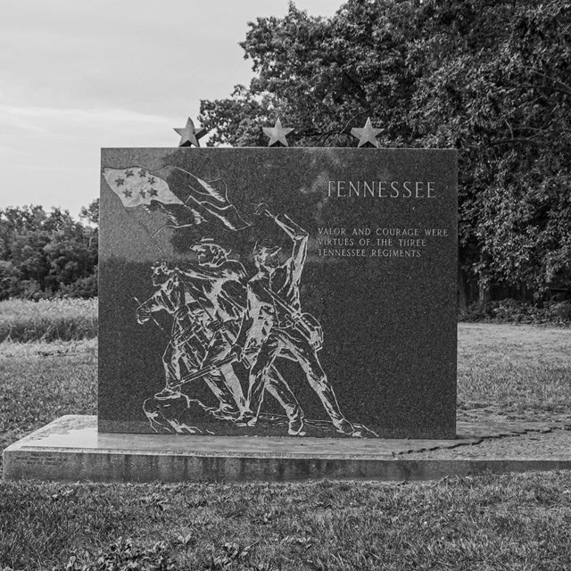 A black and white photo of a monument with an illustration of three soldiers etched in stone.