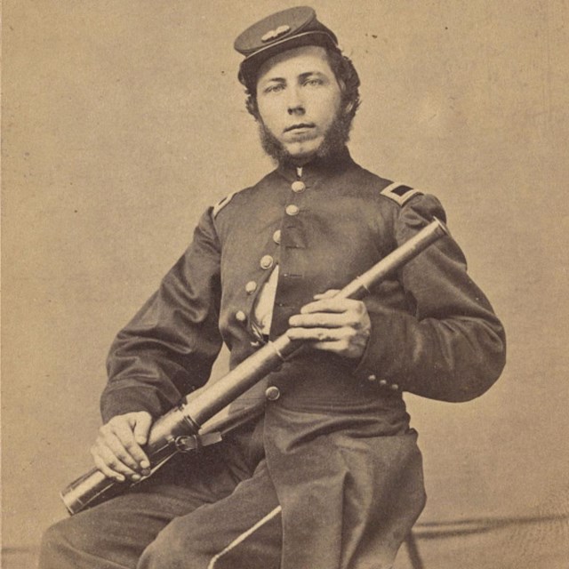 A United States Soldier seated holding a telescope