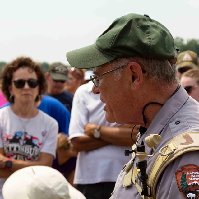 A park ranger speaks to a large group of visitors outside in a field.