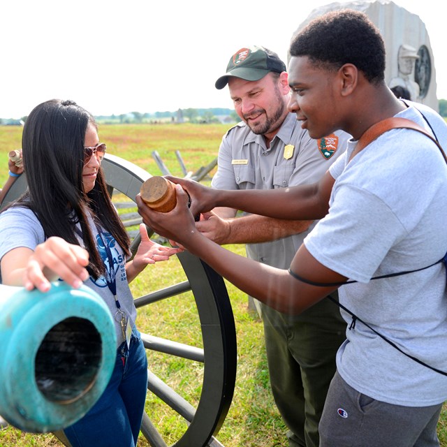 A park ranger demonstrates how to load and fire a cannon with a Great Task Experience group.