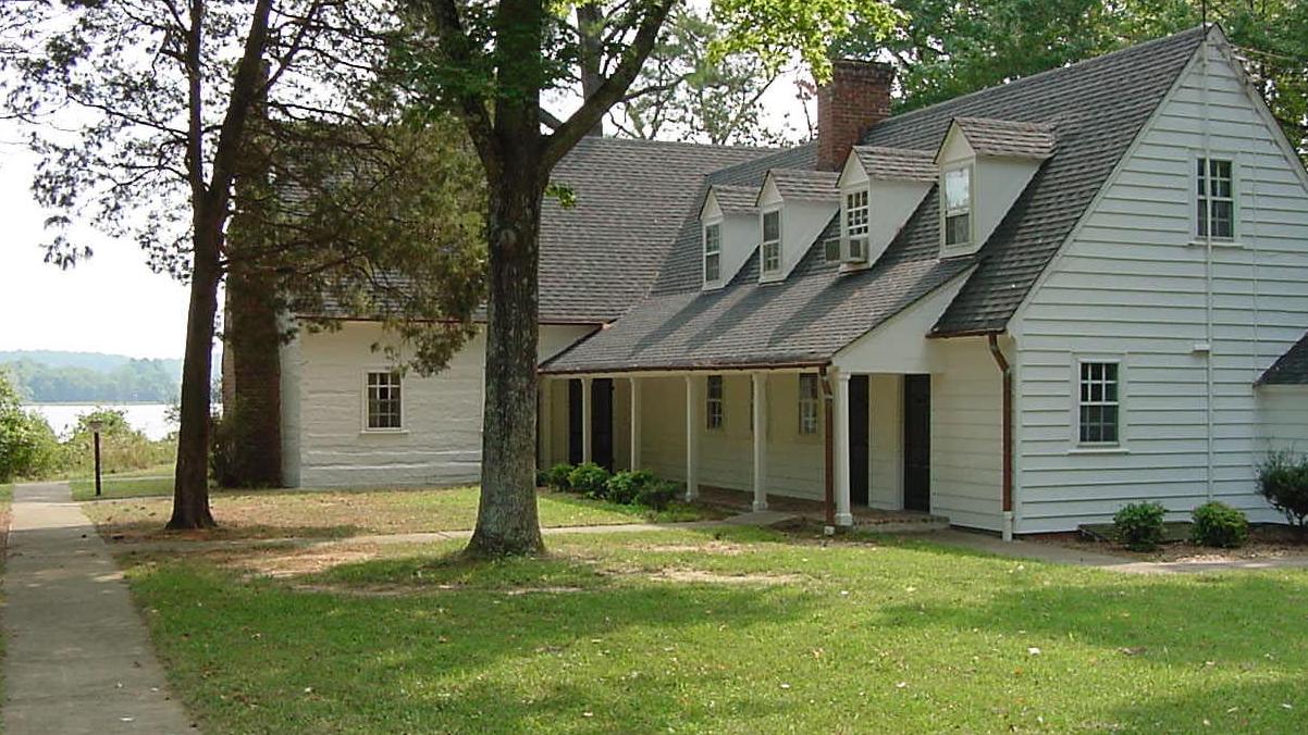 A white house surrounded by trees. Text reads, "The Log House"