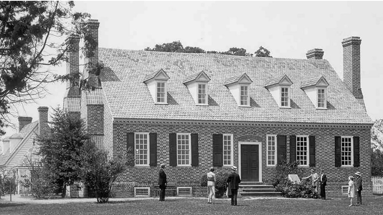 A black and white photo of a brick house with people walking towards it