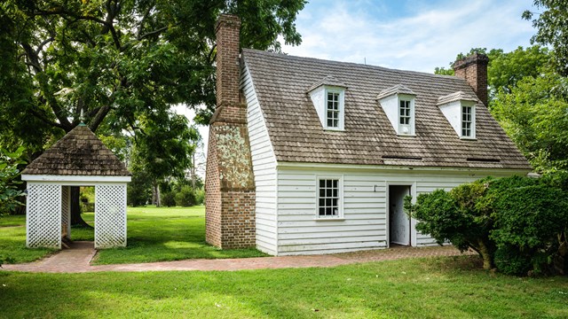 A white colonial style house next to a pavilion with a brick path.