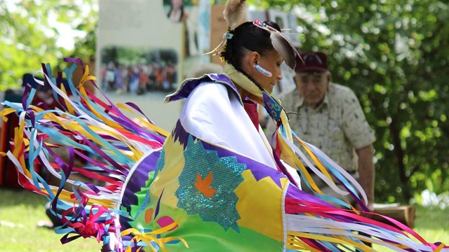 indigenous person in colorful regalia dancing in the memorial area of the park