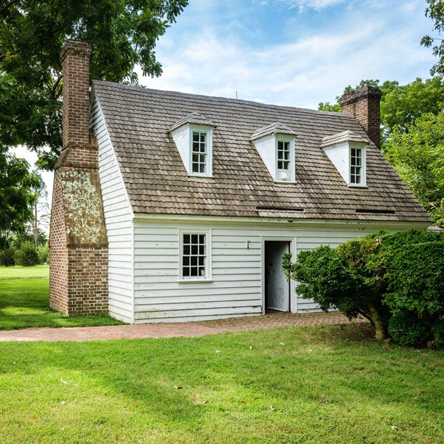 A white colonial style house next to a pavilion with a brick path.