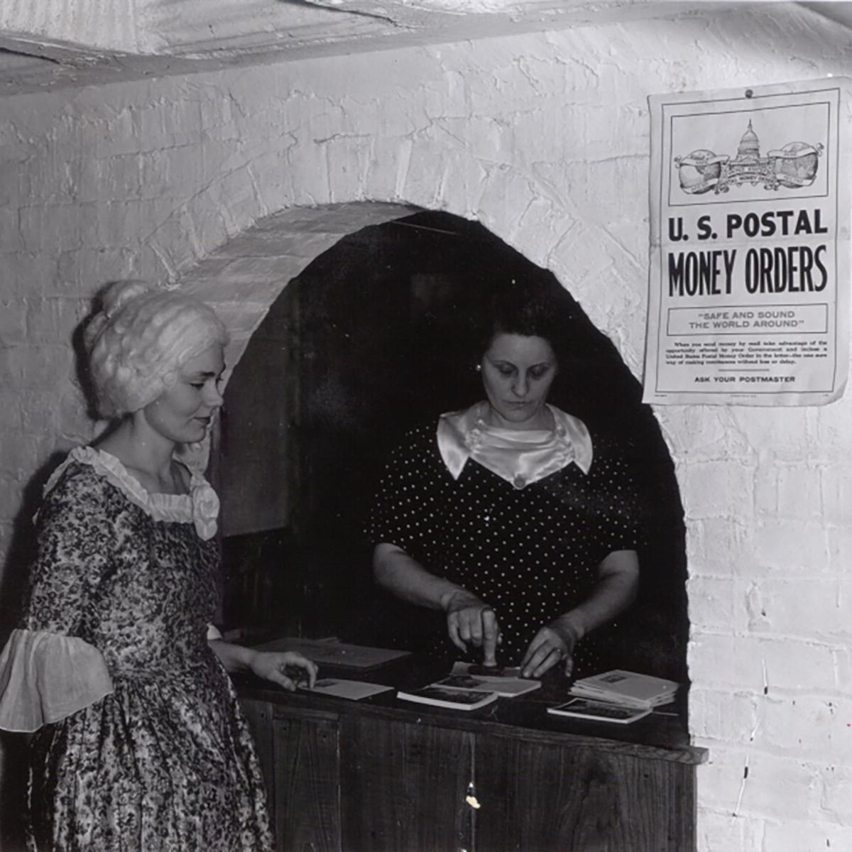 1930s photo of two women dressed in colonial clothing in a post office.