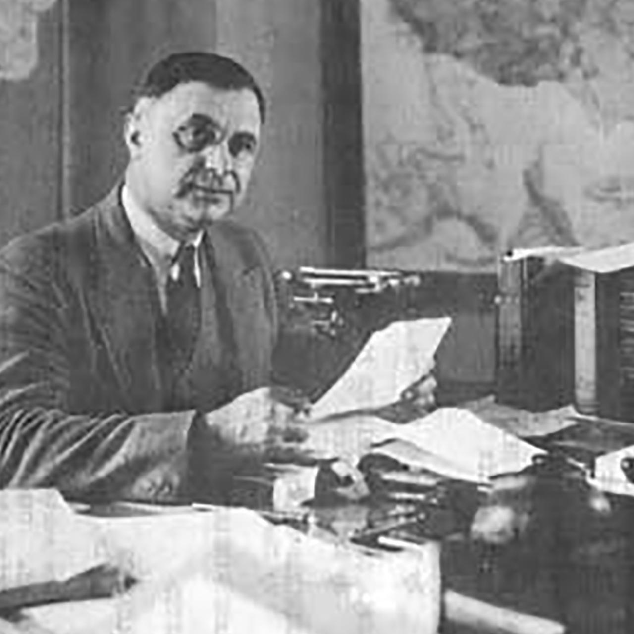 Arno Cammerer sitting at desk looking at us holding a paper in hand