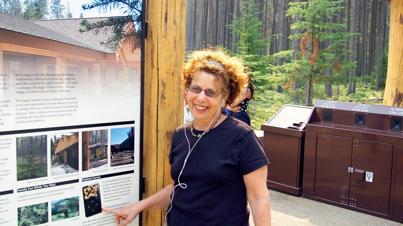 A woman wearing earbuds points to podcast information on shuttle sign