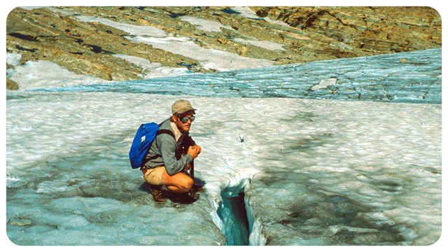 a person with a backpack crouches on glacier ice