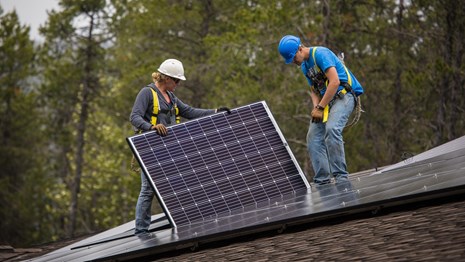 People install a solar panel on the roof of a building. 